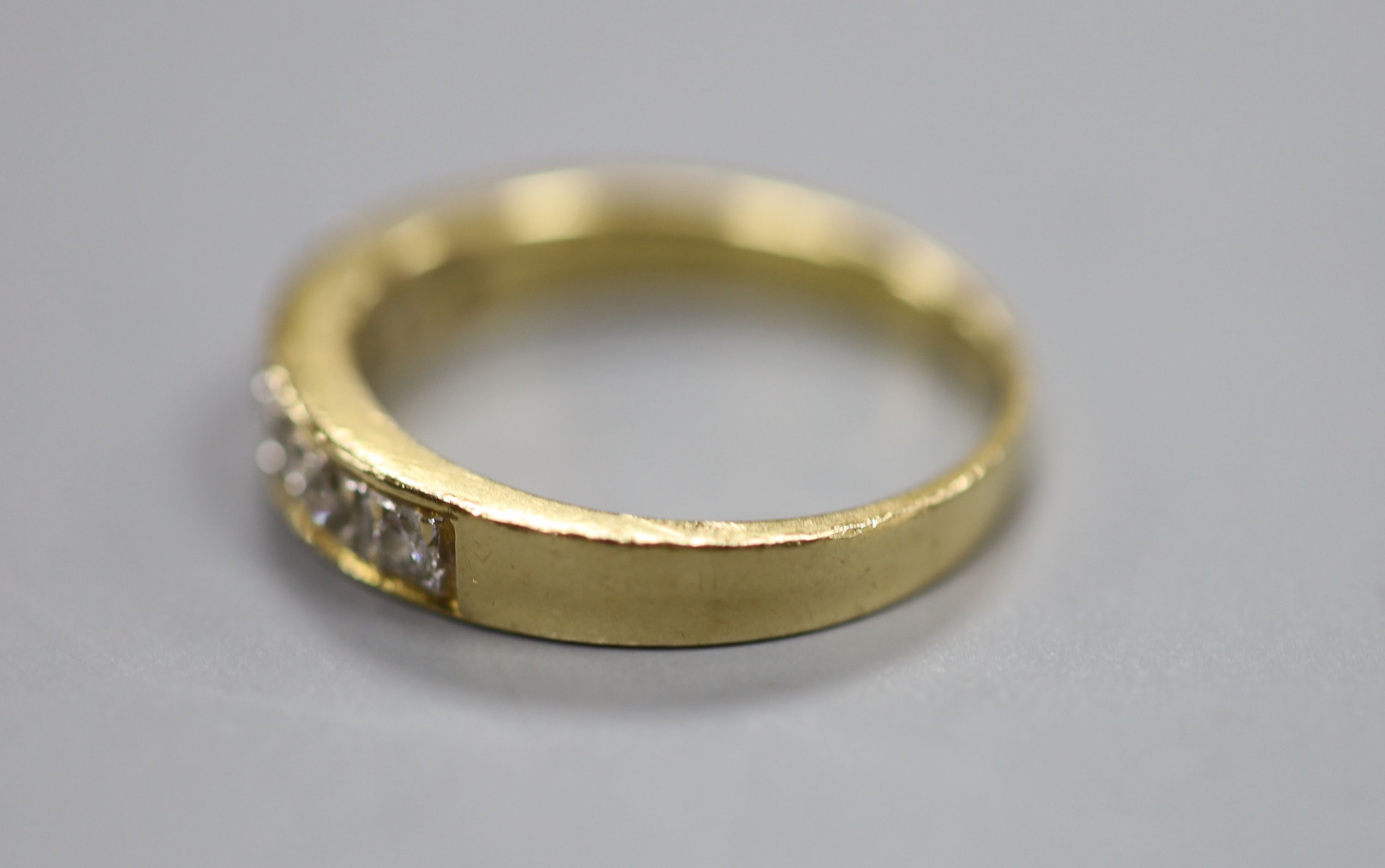 A modern 750 yellow metal and channel set seven stone diamond half hoop ring, size N, gross 3.9 grams.
